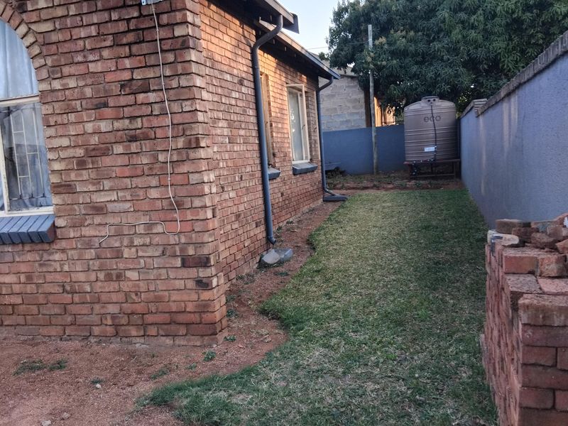 Rear exterior view of the property featuring face brick walls, a satellite dish, and a water storage tank situated in the side garden area.