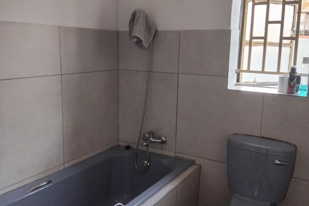 A functional bathroom featuring a grey bathtub, matching toilet, and neutral wall tiling with security bars on the window.