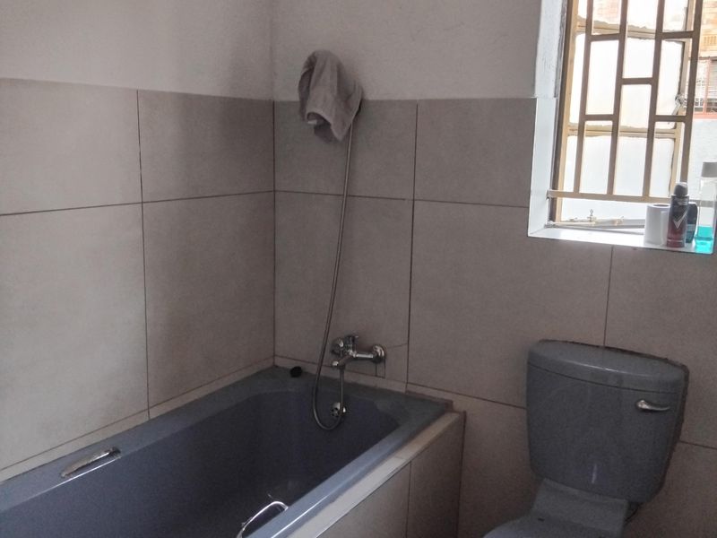 A functional bathroom featuring a grey bathtub, matching toilet, and neutral wall tiling with security bars on the window.
