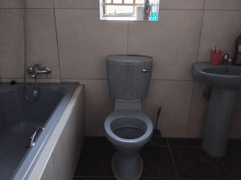 A functional bathroom featuring a bathtub, pedestal basin, and toilet with tiled finishes and a window with security bars.