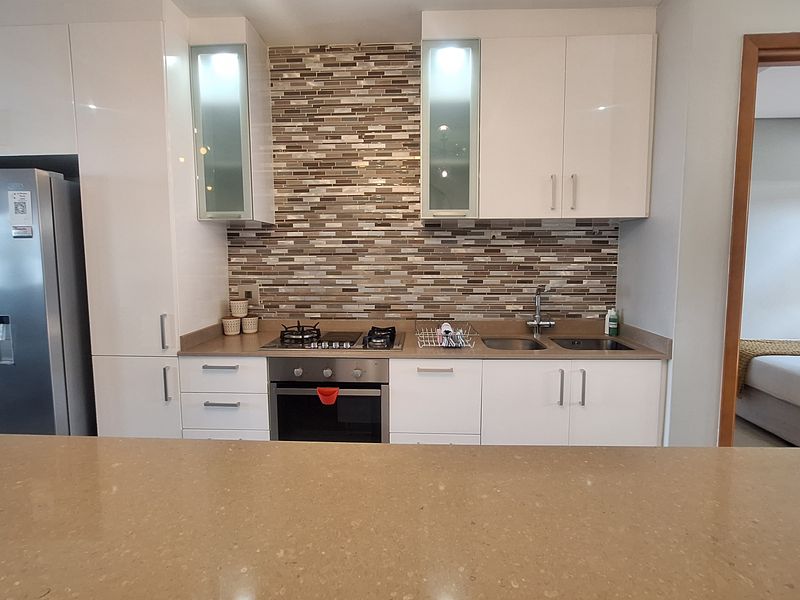 Modern kitchen featuring white cabinetry, stone countertops, a mosaic tile backsplash, and integrated stainless steel appliances, including a gas hob and oven.