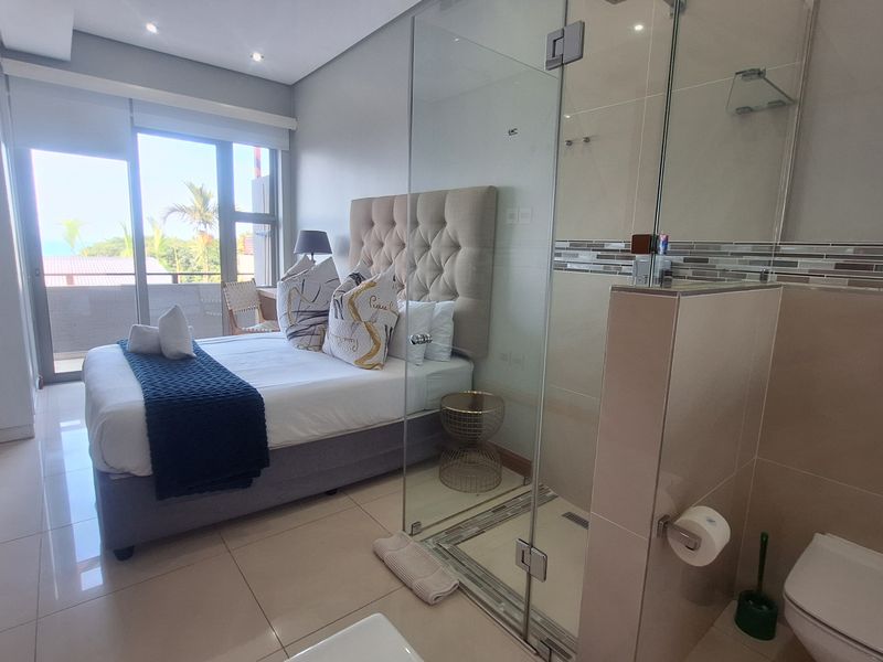 Modern bedroom featuring an open-plan en-suite bathroom with a glass shower enclosure and wall-mounted toilet, with direct access to a private balcony.