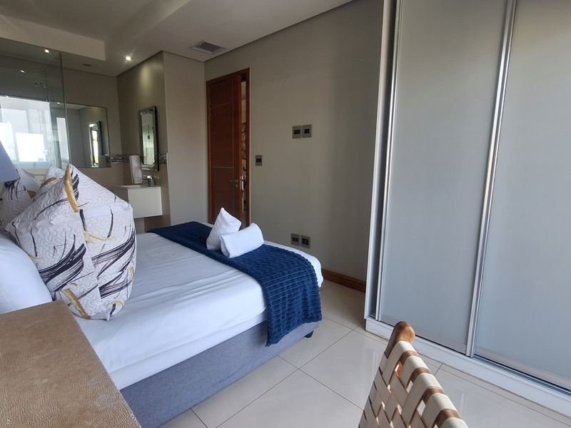 A modern bedroom featuring tiled flooring, built-in sliding door wardrobes, and an integrated en-suite bathroom with contemporary finishes.