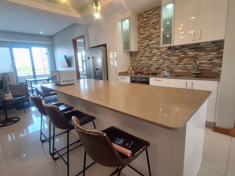 Open-plan living area featuring a modern kitchen with stone countertops, mosaic backsplash, built-in cabinetry, and a central island, seamlessly flowing into the living space.
