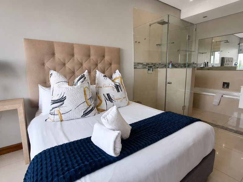 Modern bedroom featuring an open-plan en-suite bathroom with a glass shower enclosure, built-in bathtub, and wall-mounted vanity.