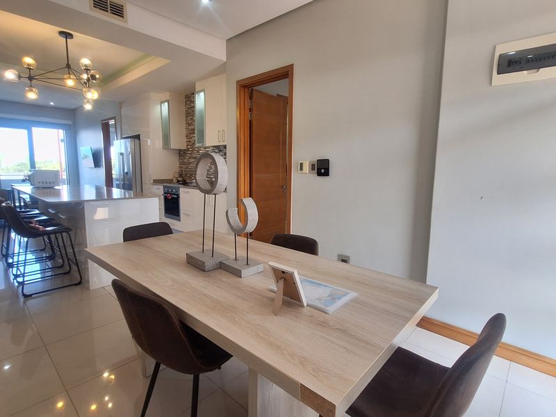 Modern open-plan living and dining area featuring a sleek kitchen island, contemporary lighting, and polished tiled flooring throughout.