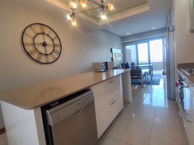 Modern open-plan kitchen and living area featuring a central island, sleek cabinetry, stone countertops, and large sliding doors leading to a balcony.
