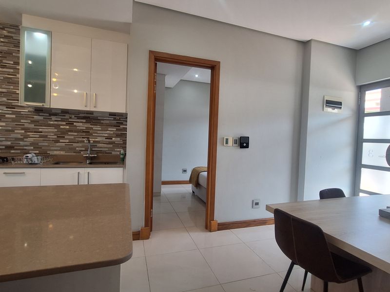 Modern open-plan kitchen and dining area featuring sleek cabinetry, stone countertops, mosaic backsplash, and tiled flooring, with seamless flow to adjacent rooms.