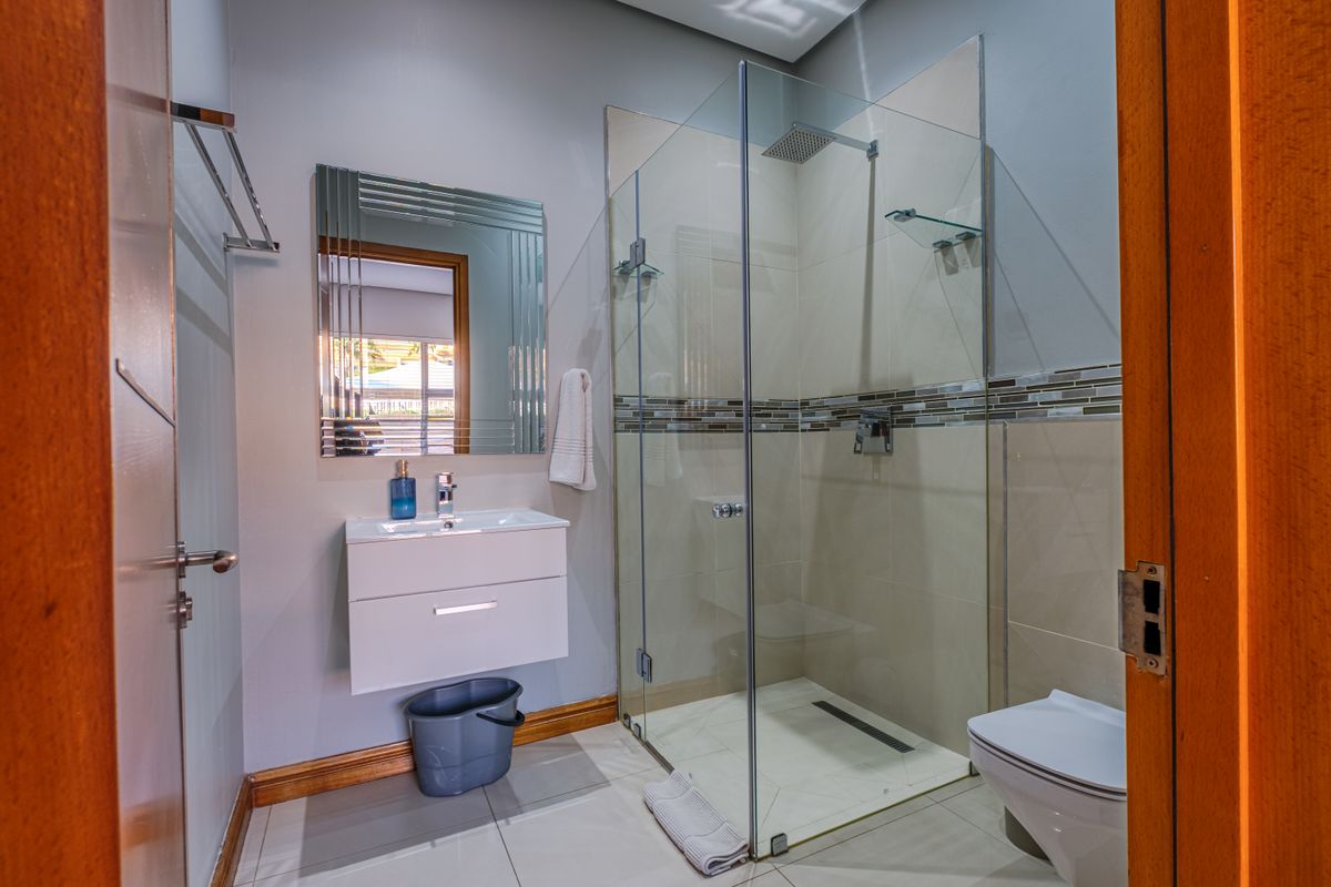 Modern bathroom featuring a wall-mounted vanity, a spacious glass-enclosed shower with a rain shower head, and a wall-hung toilet with neutral tiling.