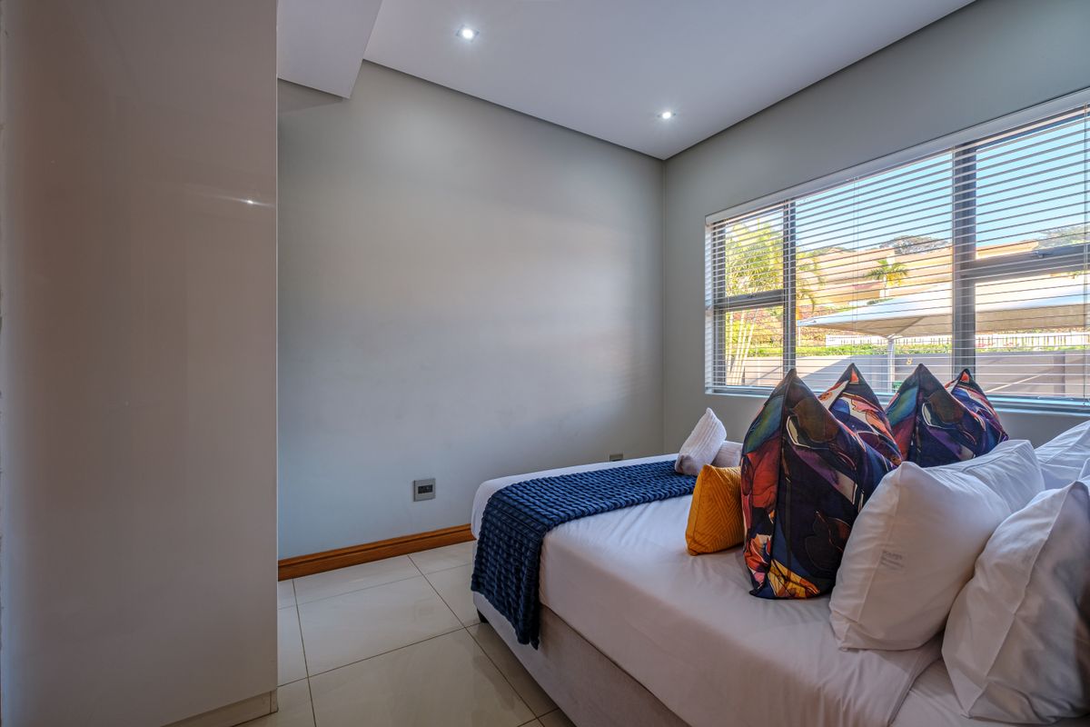 A well-maintained bedroom featuring neutral tiled flooring, recessed downlighting, and venetian blinds, offering a clean and modern aesthetic.