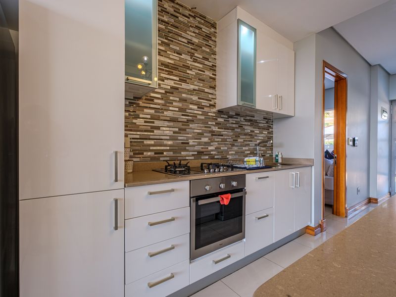 Modern kitchen featuring white high-gloss cabinetry, stone countertops, a mosaic tile backsplash, and integrated stainless steel appliances.