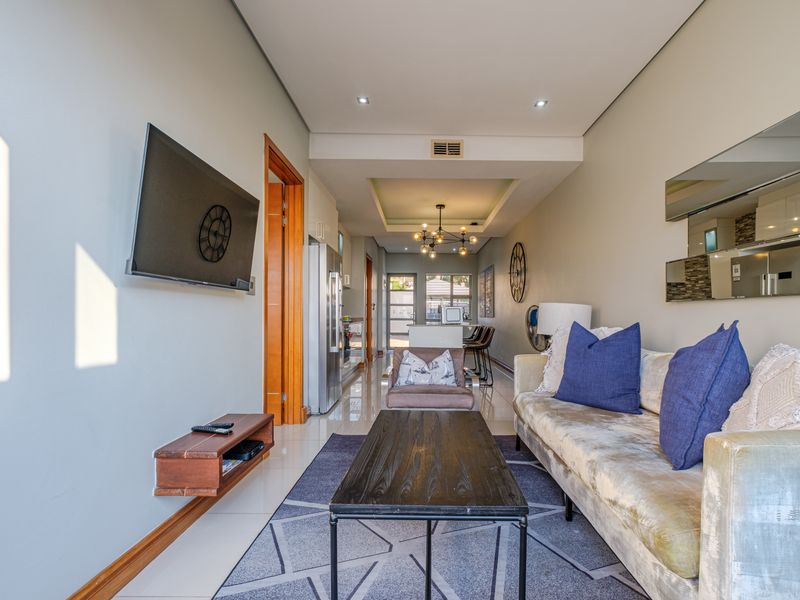 A modern open-plan living and kitchen area featuring tiled floors, recessed ceiling lighting, and a functional kitchen island with integrated cabinetry.