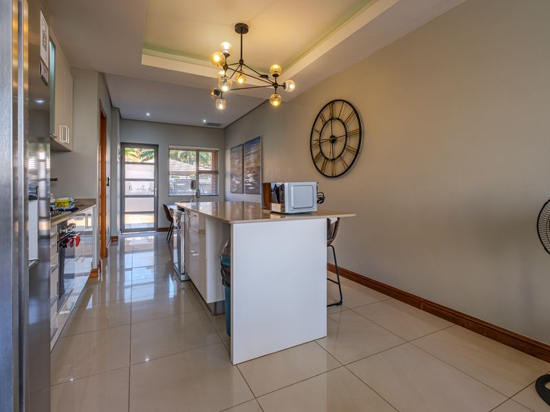 Modern kitchen featuring a central island with stone countertop, tiled flooring, and recessed lighting, leading to an exterior glass panel door.