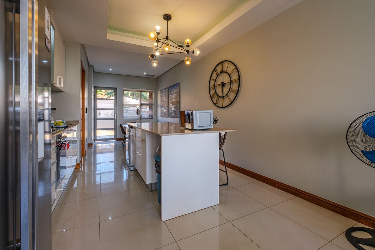 Modern kitchen featuring a central island with stone countertop, tiled flooring, and recessed lighting, leading to an exterior glass panel door.