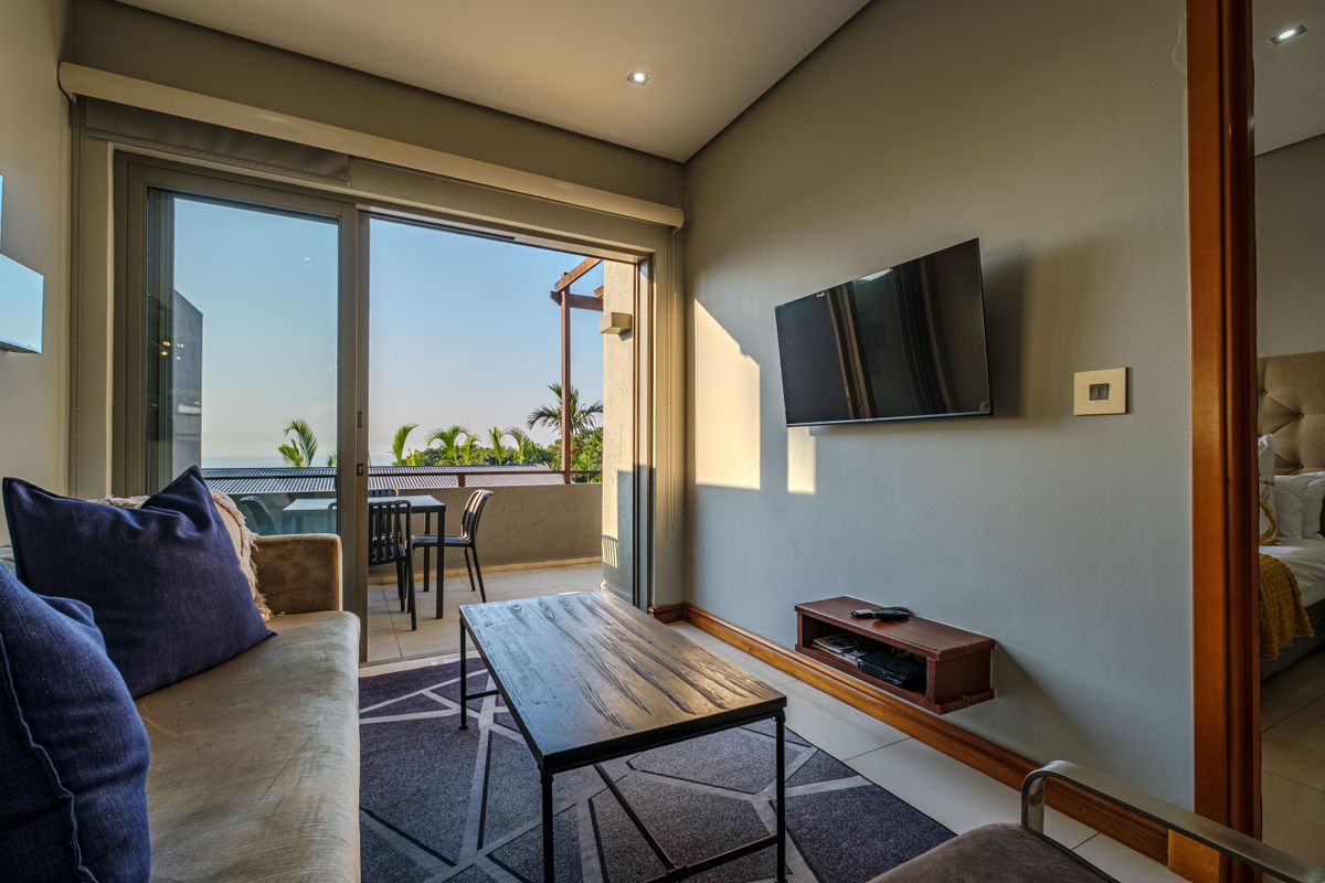 A modern living room featuring tiled floors, recessed lighting, and a large sliding glass door providing seamless access to an outdoor balcony area.