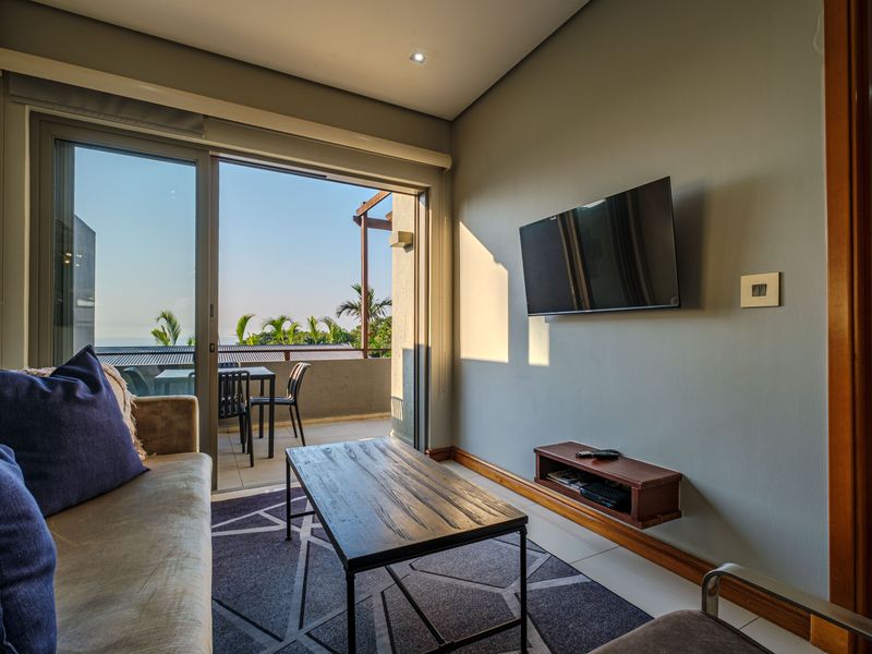 A modern living room featuring tiled floors, recessed lighting, and a large sliding glass door providing seamless access to an outdoor balcony area.