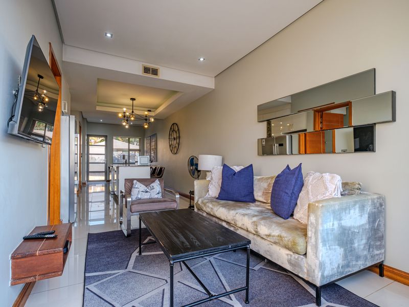 An open-plan living area featuring tiled flooring, recessed ceiling lighting, and a neutral color palette, seamlessly connecting to the kitchen space.