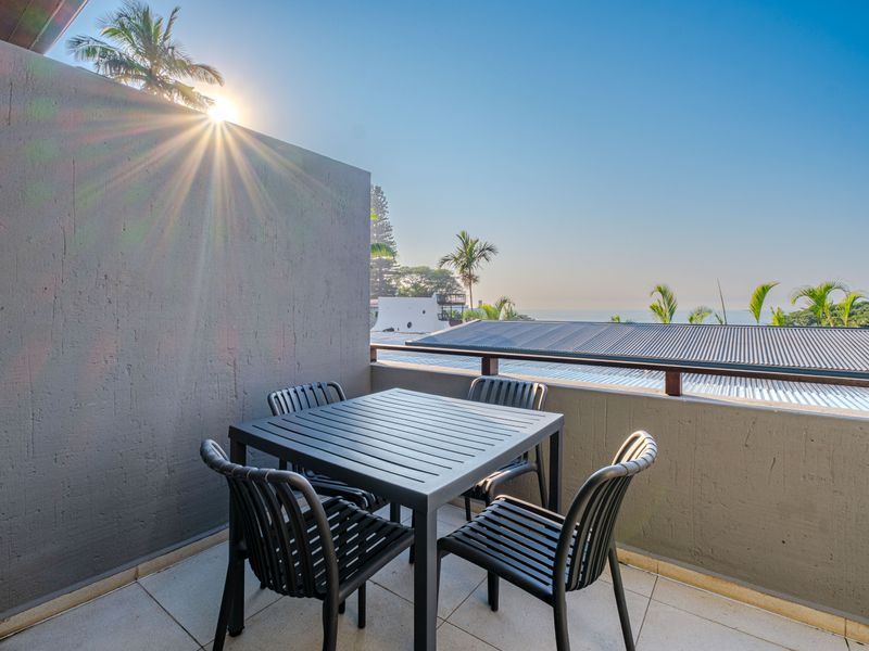 A well-maintained balcony featuring tiled flooring, a metal railing, and a textured wall, offering an open outdoor space with a clear view.