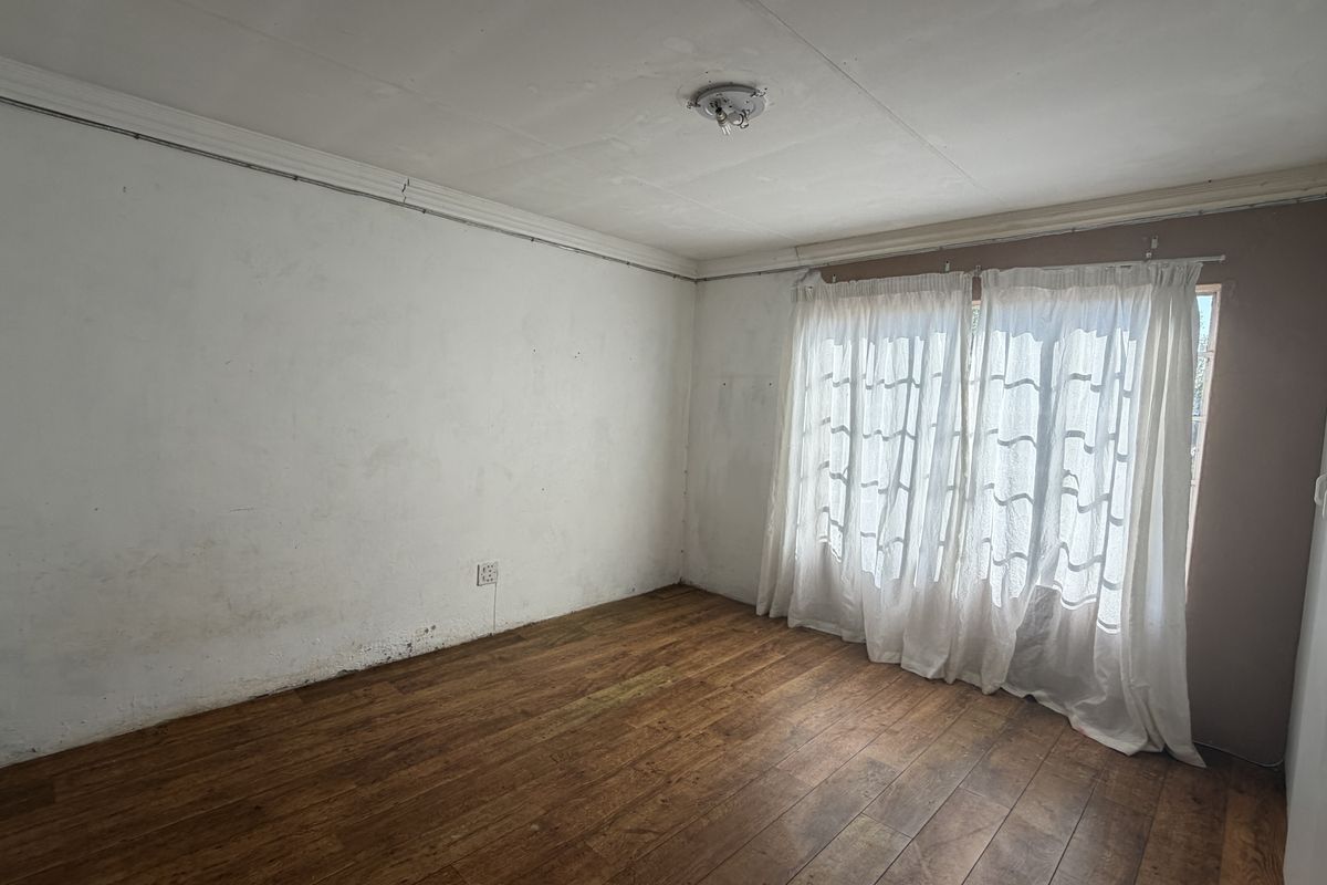 An empty bedroom featuring laminate flooring, a built-in cupboard, and large windows with curtains. The room requires cosmetic attention to walls and ceiling.