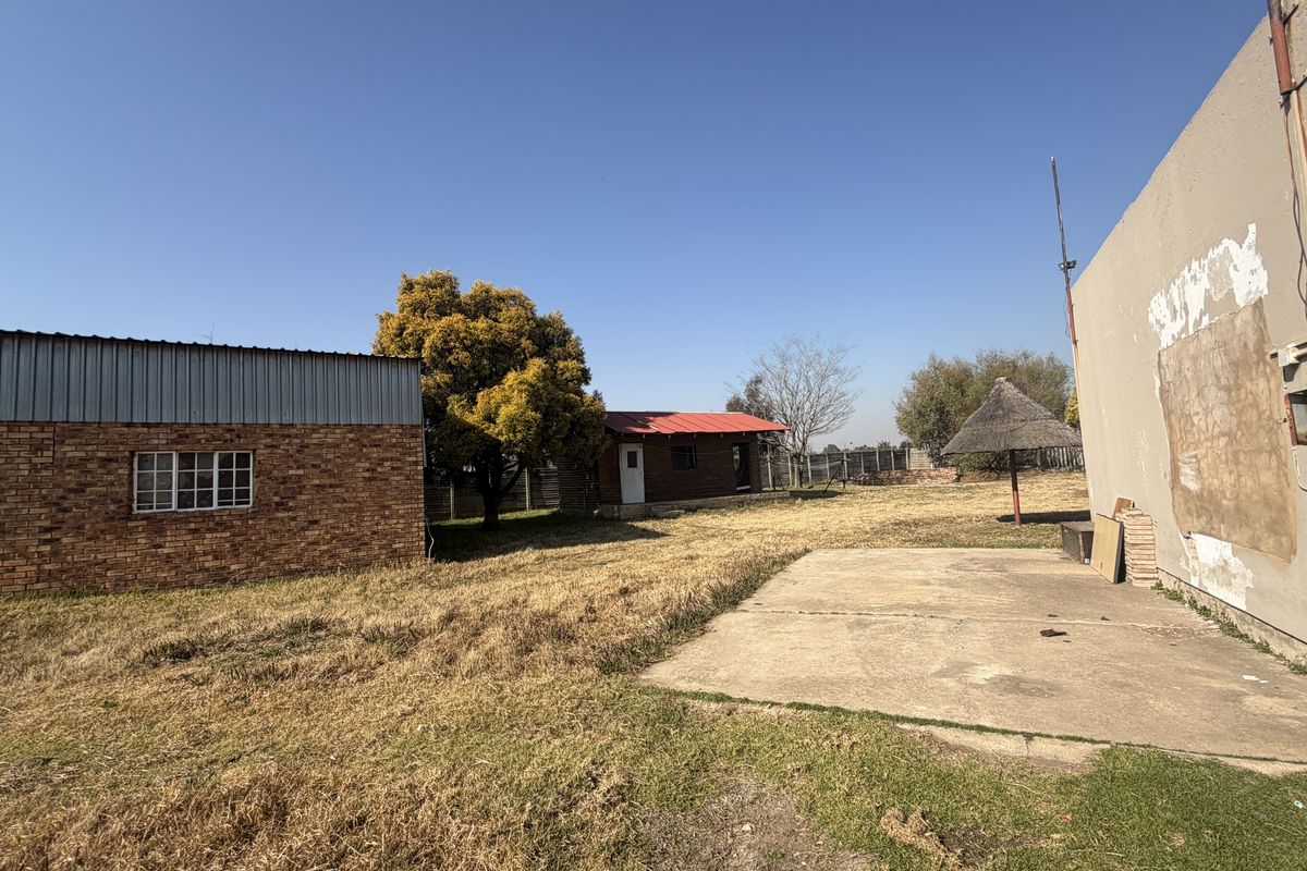 Rear exterior view of the small holding featuring facebrick outbuildings, a concrete patio area, and a large open garden space with perimeter fencing.
