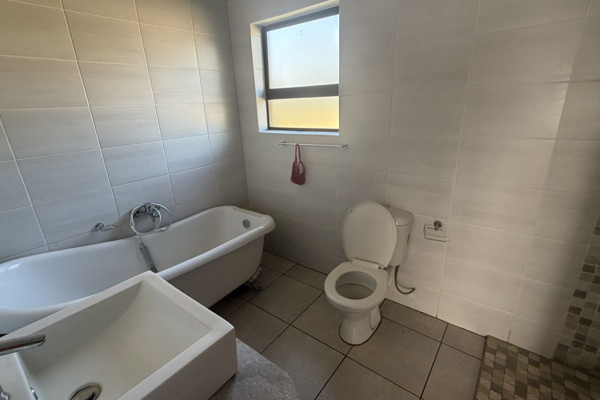 A clean, modern bathroom featuring a freestanding bathtub, a separate shower enclosure, a basin, and neutral wall and floor tiling.