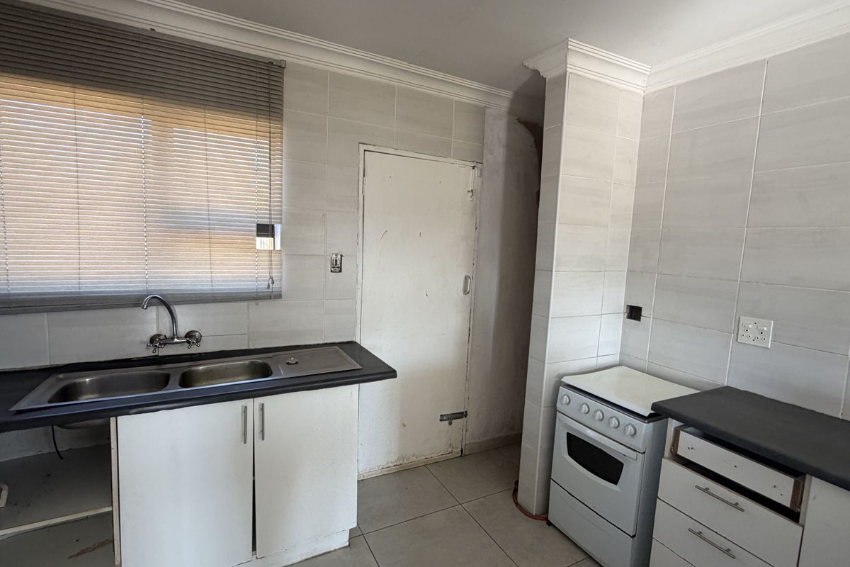 A functional kitchen featuring tiled walls, double sink, and built-in cabinetry, requiring some cosmetic repairs and updates to the finishes.