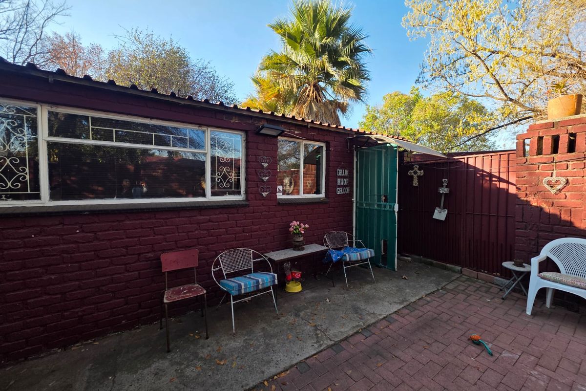 Rear exterior view of the property featuring a brick facade, paved patio area, and secure metal entrance gate.