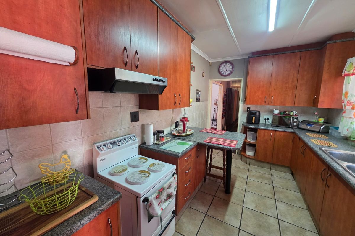 A functional kitchen featuring wooden cabinetry, laminate countertops, a freestanding stove with extractor fan, and tiled flooring.