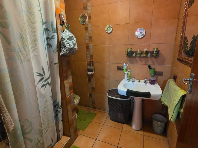 A functional bathroom featuring a pedestal sink, shower enclosure, and warm-toned ceramic wall and floor tiling.