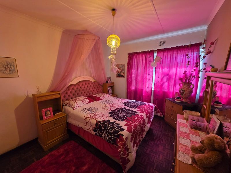 A bedroom featuring parquet flooring and a ceiling vent, currently styled with vibrant pink decor and lighting.