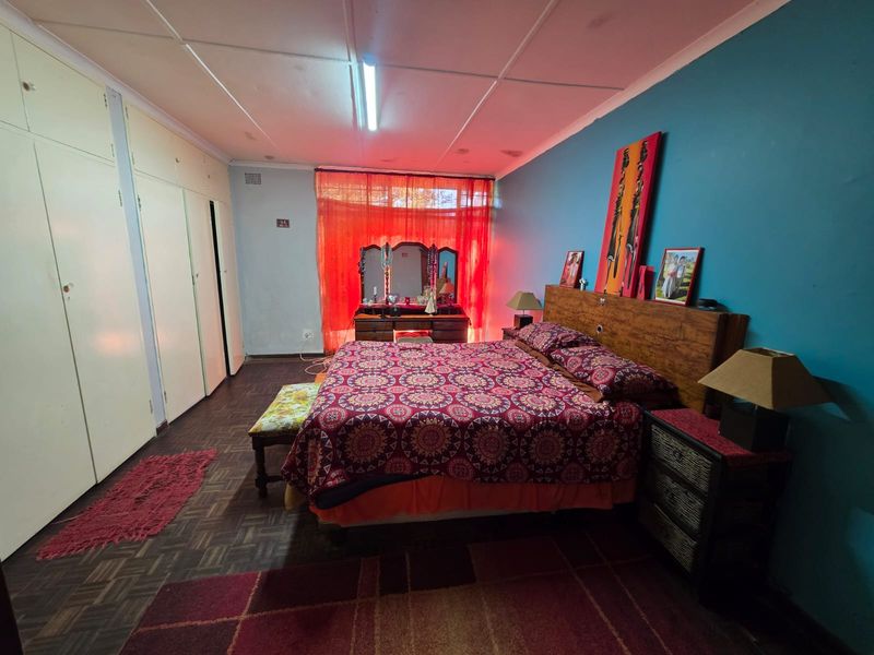 Spacious bedroom featuring built-in cupboards, parquet flooring, and ceiling tiles, offering a functional layout ready for cosmetic updates.