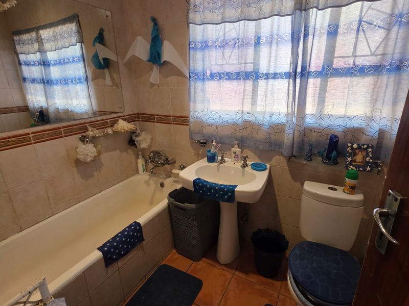 A compact bathroom featuring a pedestal basin, bathtub, and toilet with tiled walls and flooring, requiring cosmetic updates to modernize the space.