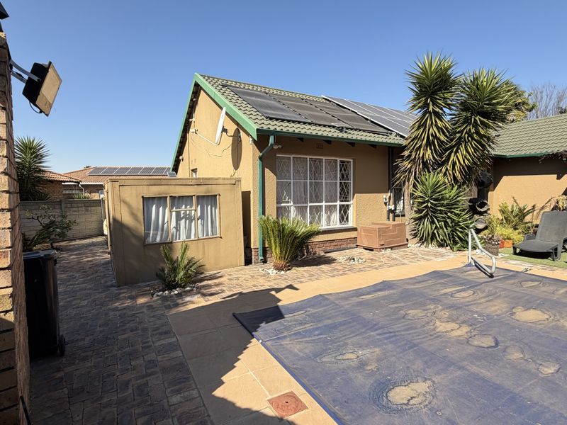 Rear exterior view featuring a swimming pool with cover, paved patio area, and a house roof equipped with solar panels.