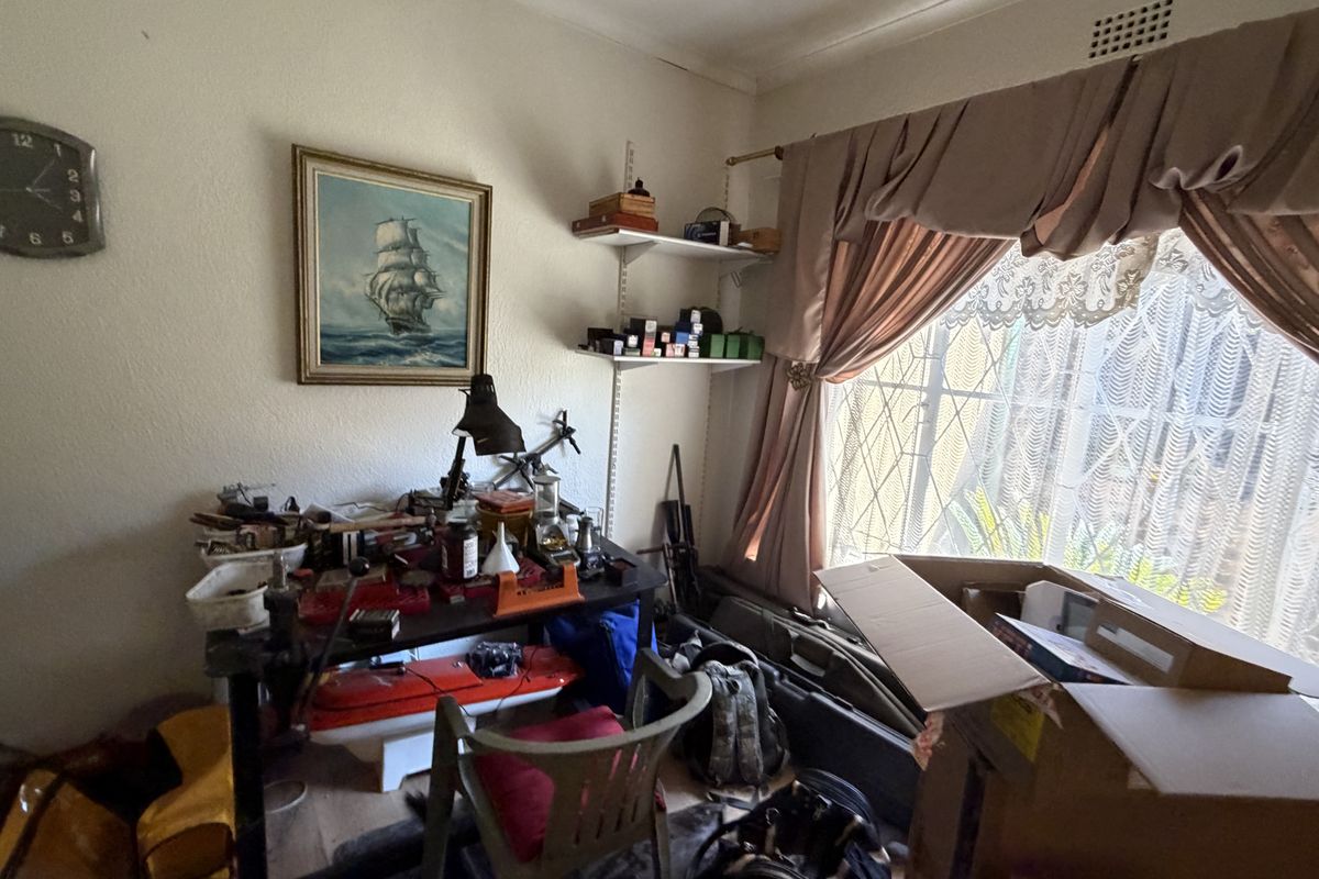 A bedroom space featuring a window with security bars and wall-mounted shelving, currently utilized as a hobby or work area.