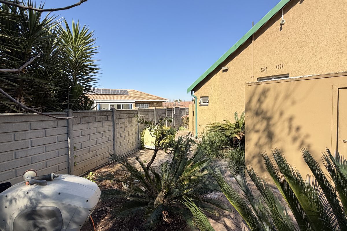A side garden pathway featuring a precast concrete boundary wall, paved flooring, and established garden landscaping along the exterior of the house.