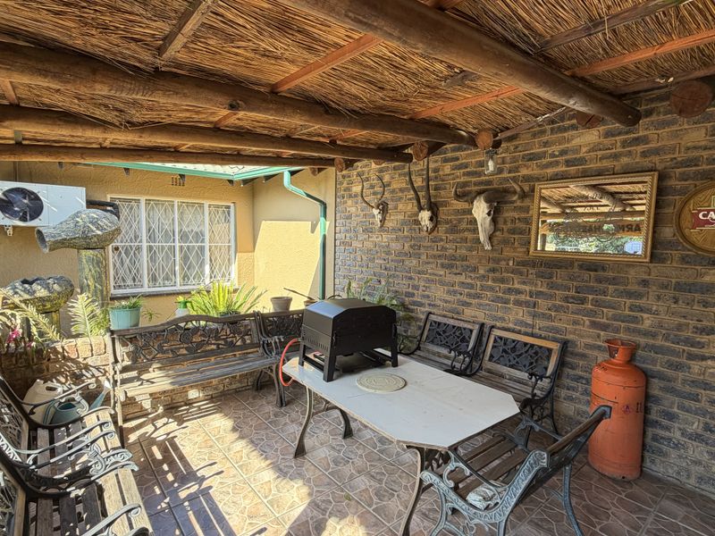 Covered outdoor patio area featuring a rustic thatched roof, exposed brick walls, and tiled flooring, providing a functional space for outdoor entertaining.