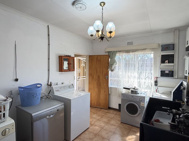 A functional laundry room featuring tiled flooring, dedicated plumbing connections, and an integrated electrical distribution board, offering potential for modernization and improved utility layout.