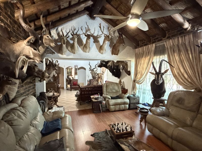 Spacious living room featuring a high vaulted ceiling with exposed timber beams, thatched roof detail, exposed brick walls, and tiled flooring.