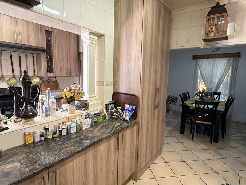 Open plan kitchen and dining area featuring wood-look cabinetry, granite countertops, and ceramic floor tiles with a decorative column accent.