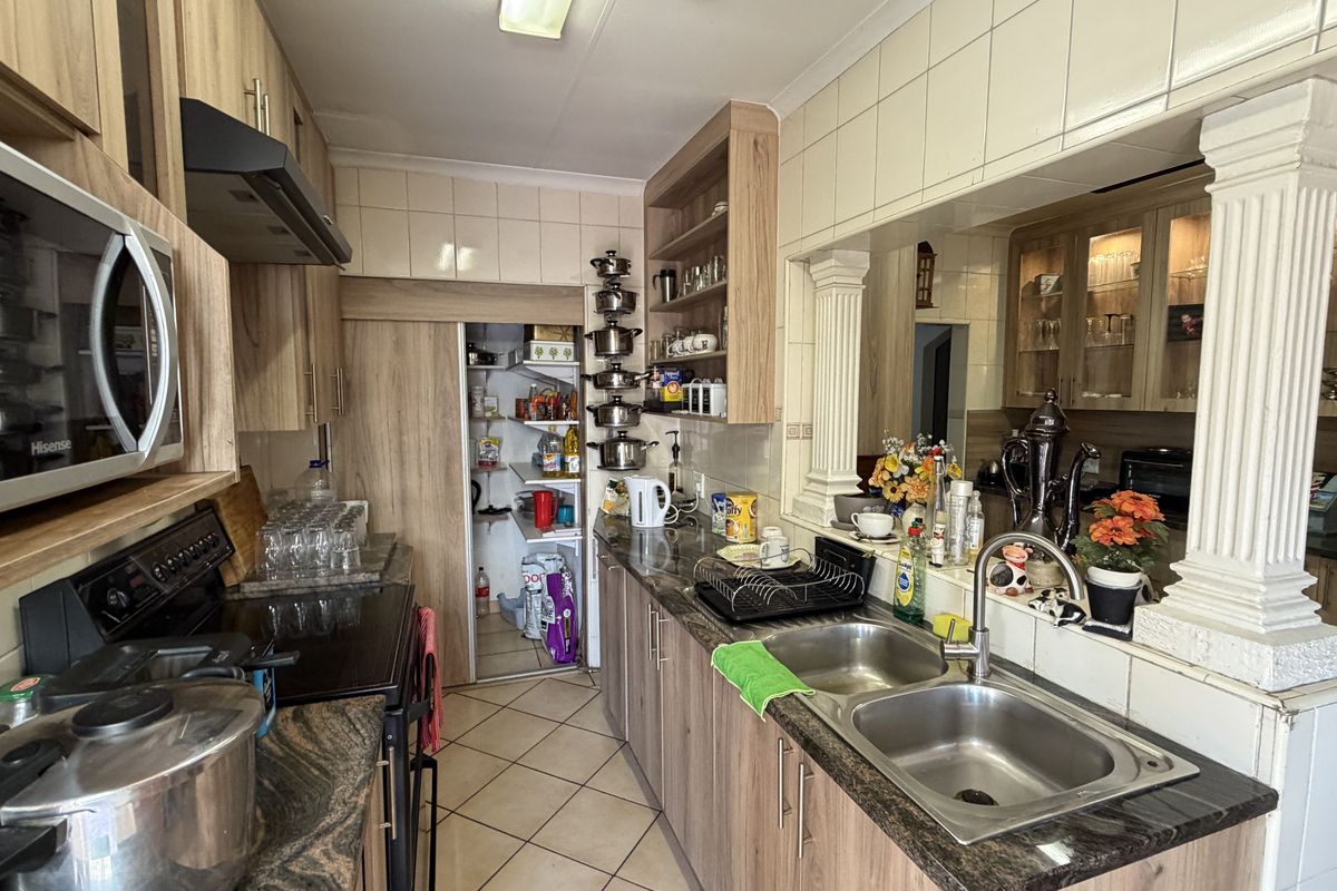 A functional kitchen featuring wood-look cabinetry, granite-style laminate countertops, a double stainless steel sink, and a dedicated pantry area with tiled splashbacks.