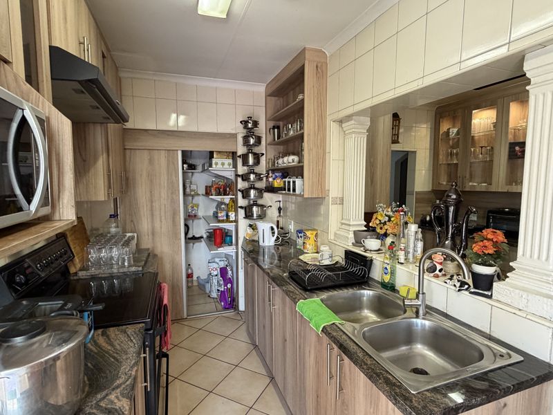 A functional kitchen featuring wood-look cabinetry, granite-style laminate countertops, a double stainless steel sink, and a dedicated pantry area with tiled splashbacks.