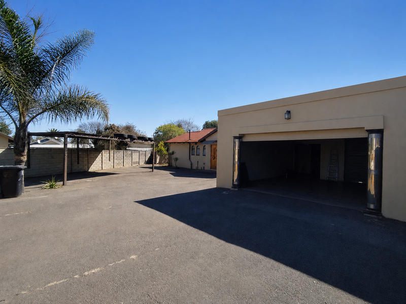 Spacious paved driveway featuring a double garage, additional carport structure, and secure boundary walling, providing ample off-street parking space.