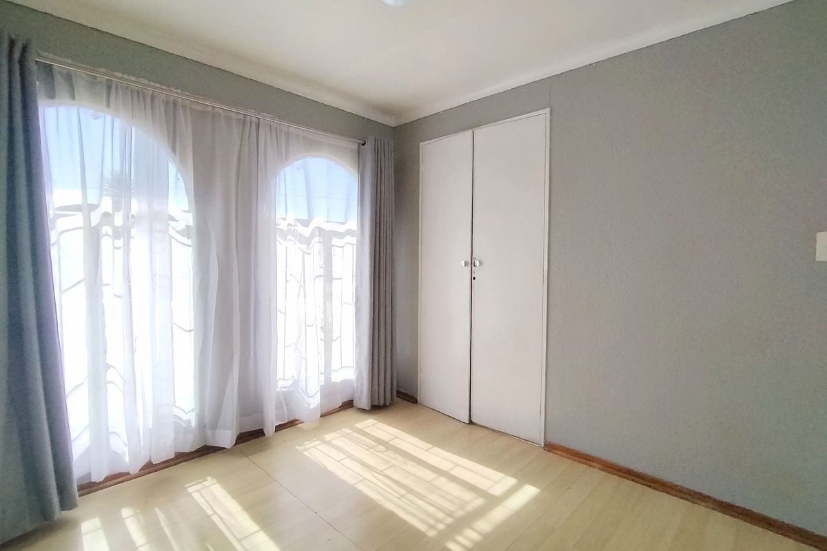 A bright, empty bedroom featuring laminate flooring, built-in wardrobe storage, and distinctive arched windows allowing for ample natural light.