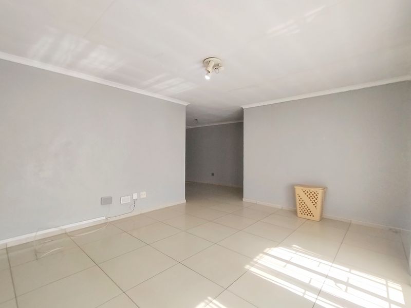 An empty, neutrally painted living area featuring tiled flooring and ceiling-mounted lighting, offering a blank canvas for interior design.