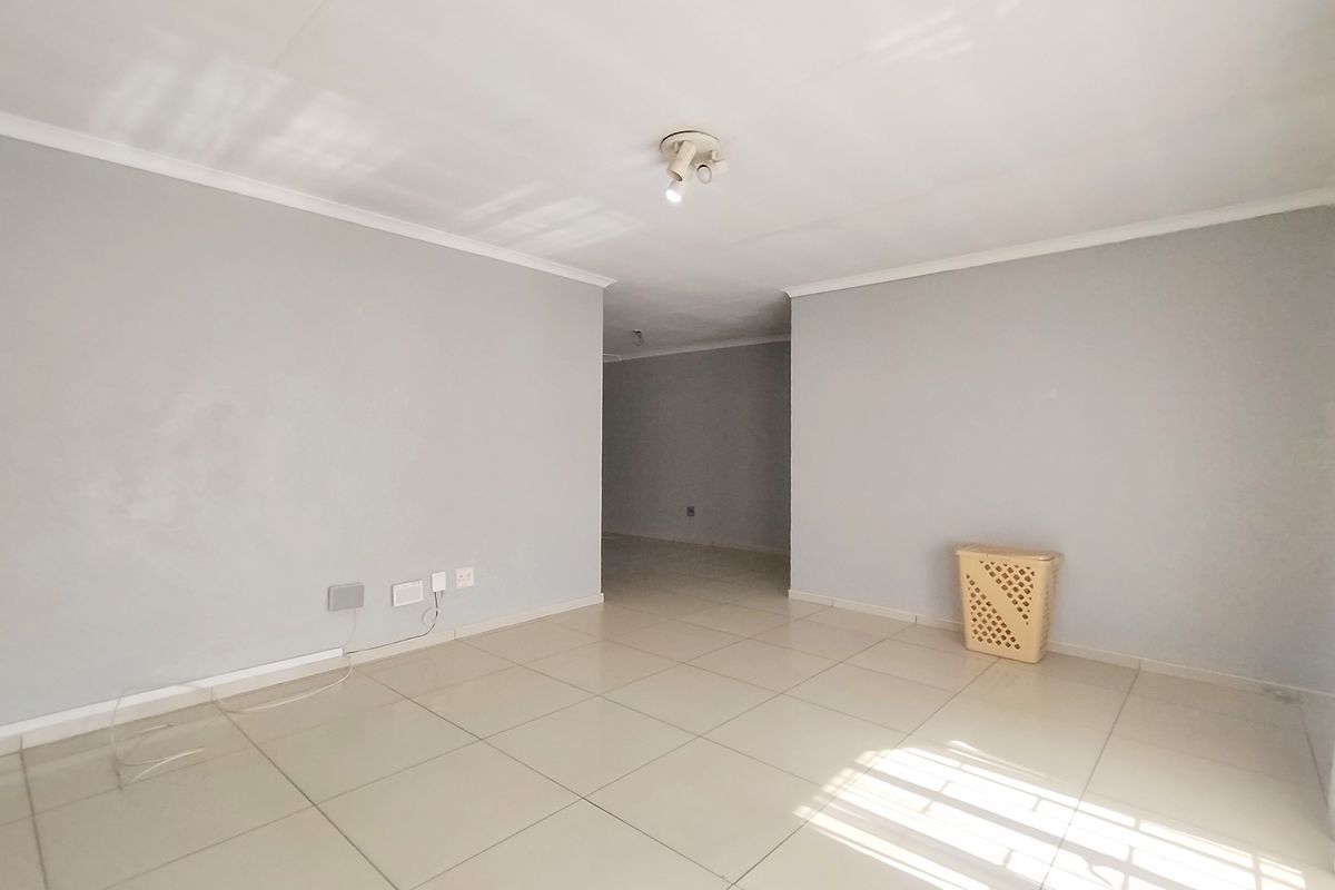 An empty, neutrally painted living area featuring tiled flooring and ceiling-mounted lighting, offering a blank canvas for interior design.