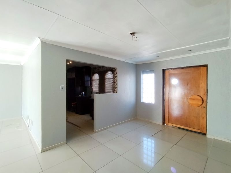 An open-plan entry area featuring polished floor tiles, a solid wood front door, and a pass-through opening leading into the kitchen space.