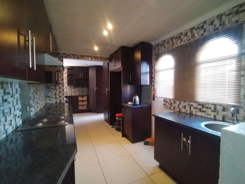 A functional kitchen featuring dark wood cabinetry, granite countertops, mosaic tile backsplash, and built-in cooking appliances with tiled flooring throughout.