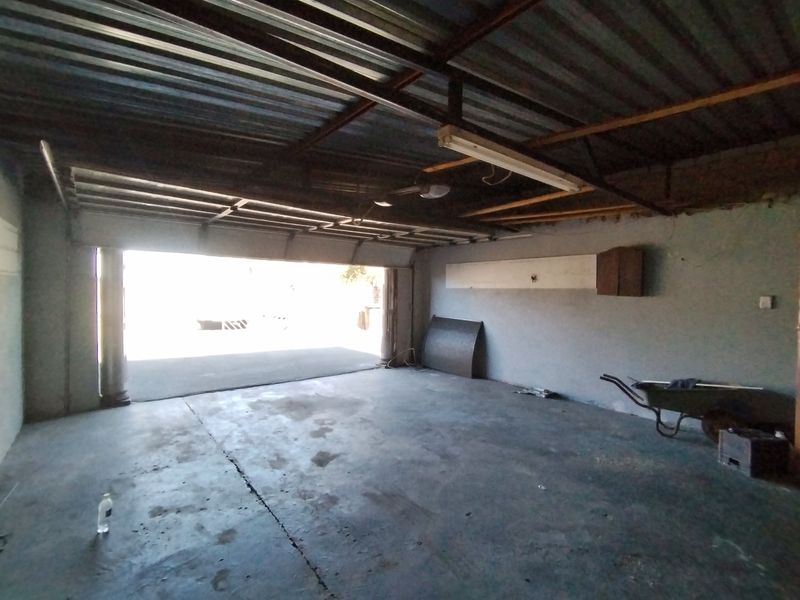A spacious, unfinished garage featuring exposed steel roof trusses, corrugated metal roofing, and concrete flooring, offering ample storage or parking potential.