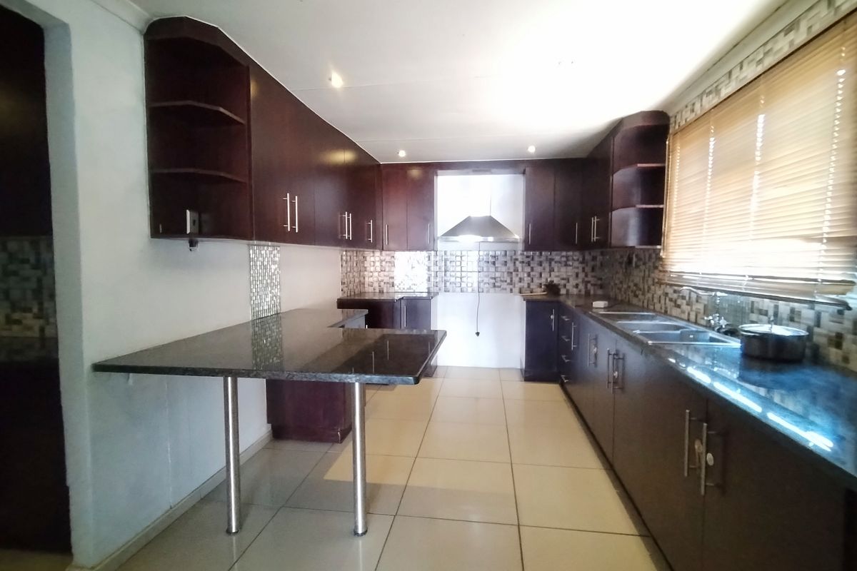 A spacious kitchen featuring dark wood cabinetry, granite countertops, a breakfast bar, and a stainless steel extractor fan with neutral tiled flooring.