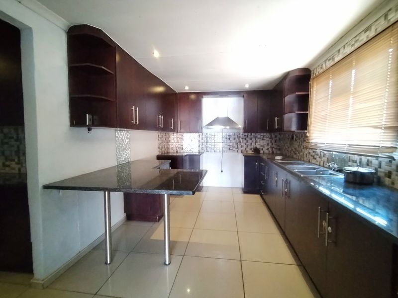 A spacious kitchen featuring dark wood cabinetry, granite countertops, a breakfast bar, and a stainless steel extractor fan with neutral tiled flooring.